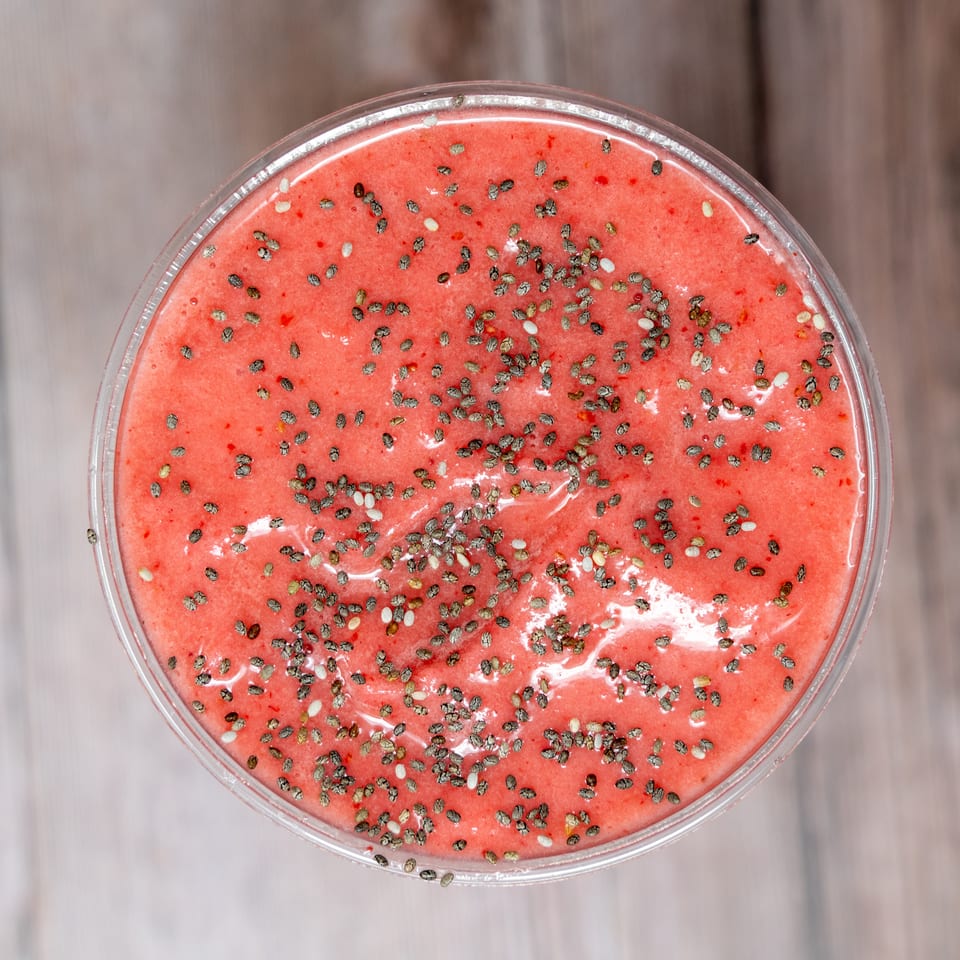 Top-down view of a bright pink smoothie in a clear bowl, sprinkled generously with chia seeds.