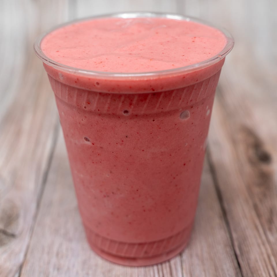 Pink berry smoothie in a clear plastic cup on a light wooden table.