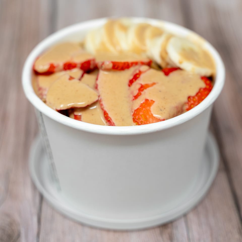 Bowl of sliced strawberries drizzled with creamy sauce and topped with sliced bananas on a wooden table.