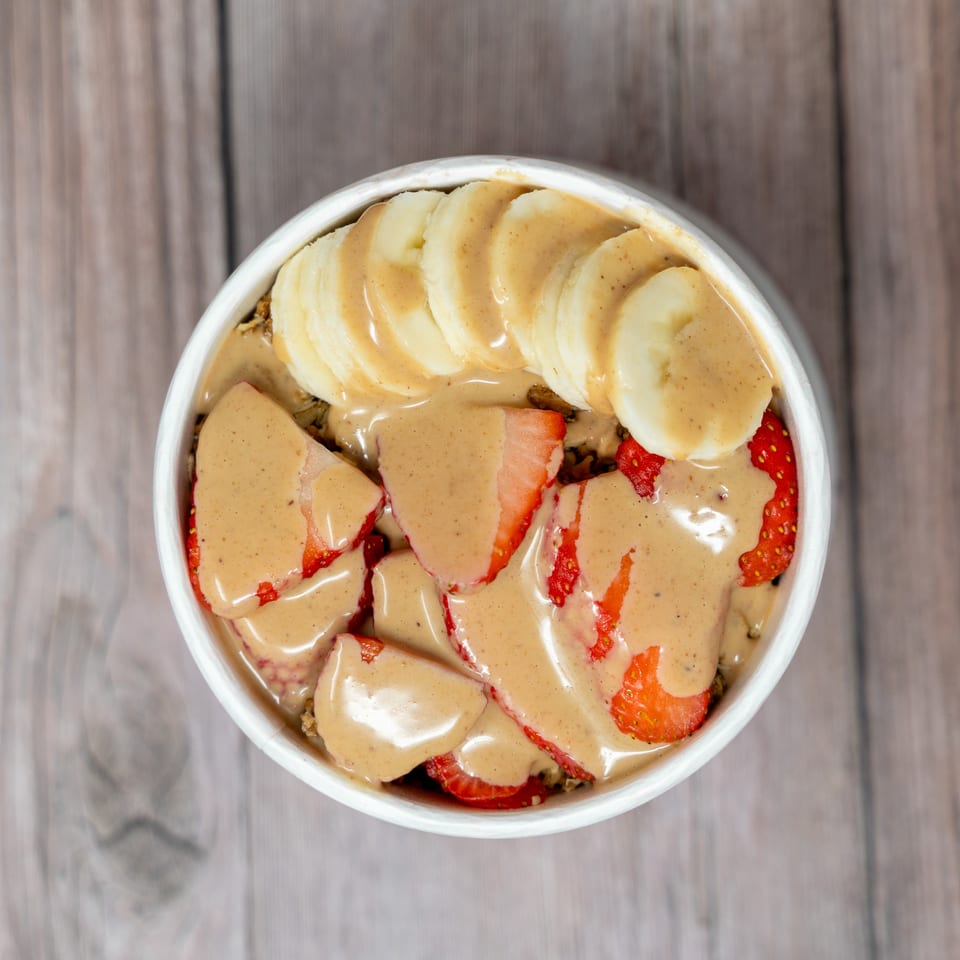 Bowl of sliced strawberries and bananas topped with creamy peanut butter sauce on a wooden table.