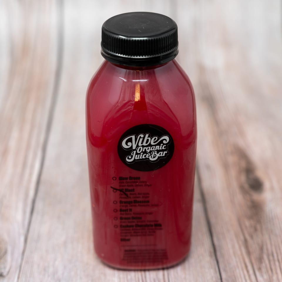 Bottle of red organic juice from Vibe Organic Juice Bar on a wooden table.