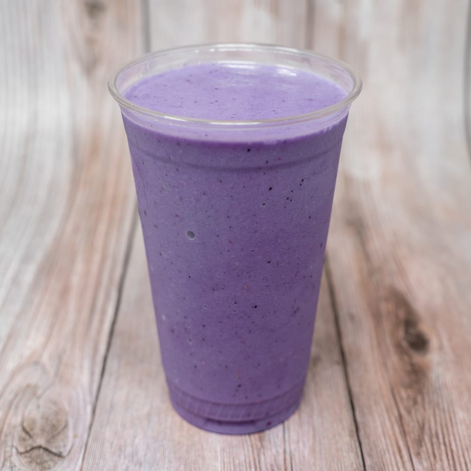 Purple berry smoothie in a clear plastic cup on a rustic wooden table.