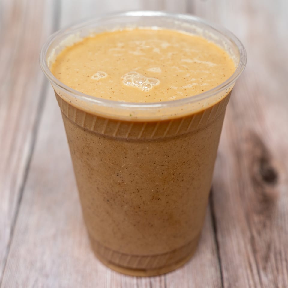 A foamy, speckled brown beverage fills a clear plastic cup on a wooden table.