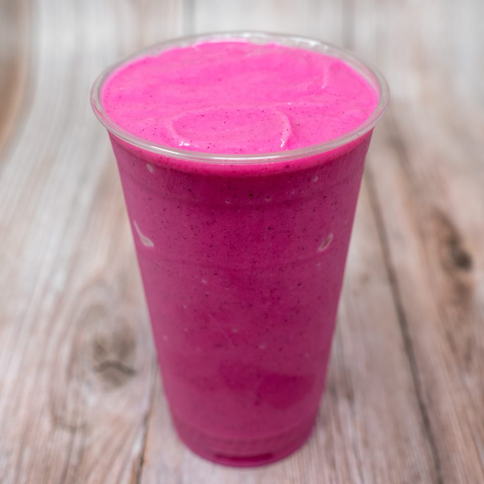 Bright pink blended smoothie in a clear plastic cup on a light wooden table.