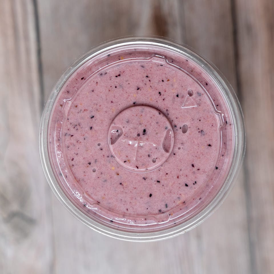 Top-down view of a clear container filled with pink berry-speckled smoothie on a light wooden surface.