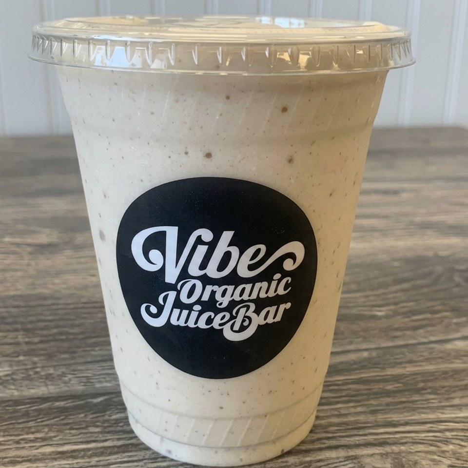 Creamy speckled smoothie in a lidded cup labeled Vibes Organic Juice Bar on a rustic wooden table.
