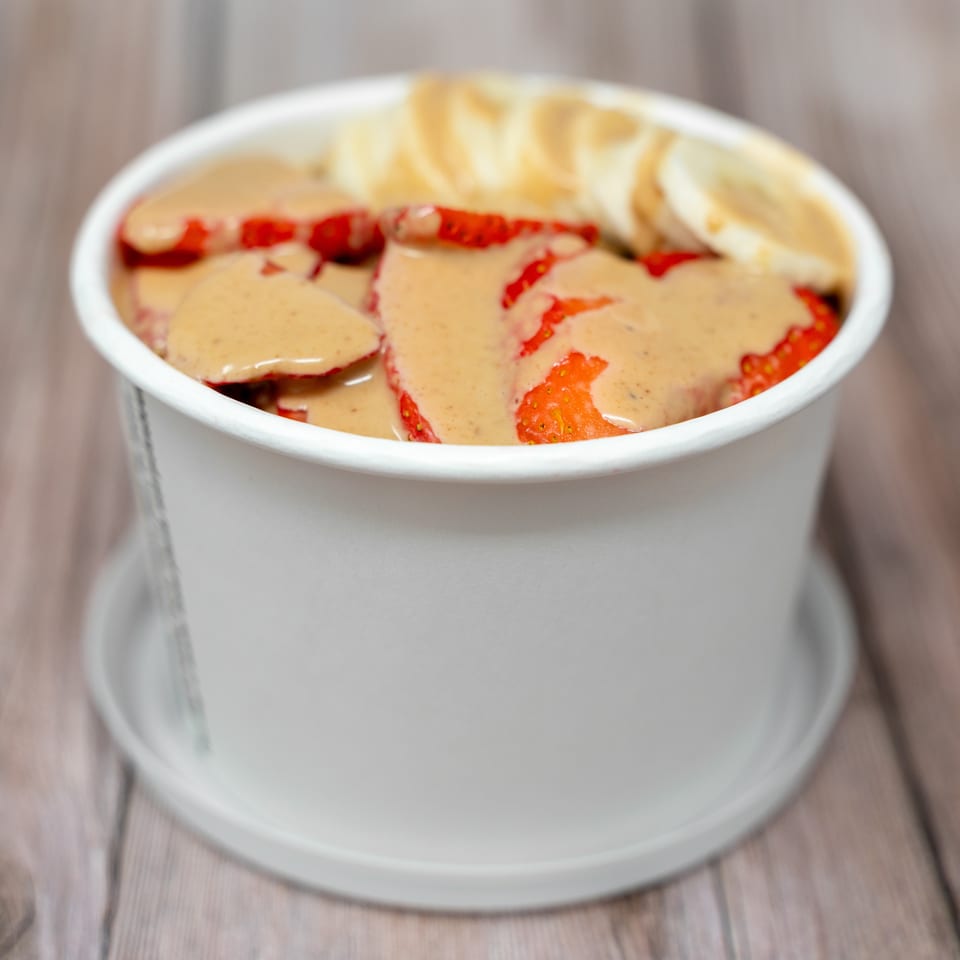 Bowl of sliced strawberries drizzled with creamy sauce, topped with folded flatbread, on a wooden table.