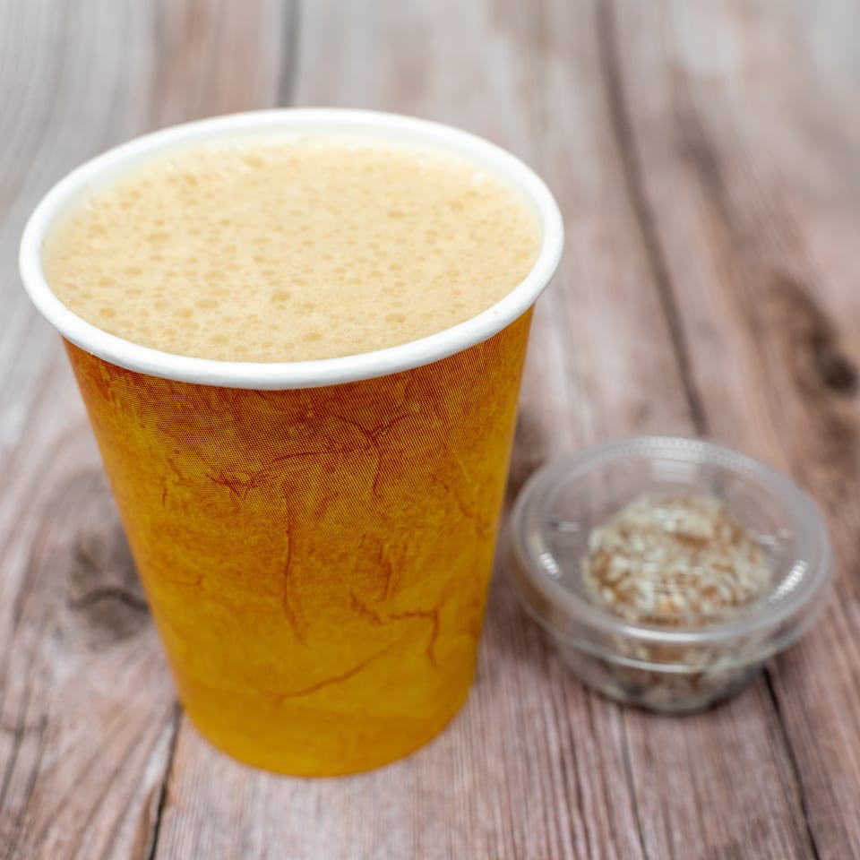 Golden foamy beverage in a textured cup sits beside a small bowl of chopped nuts on a wooden table.